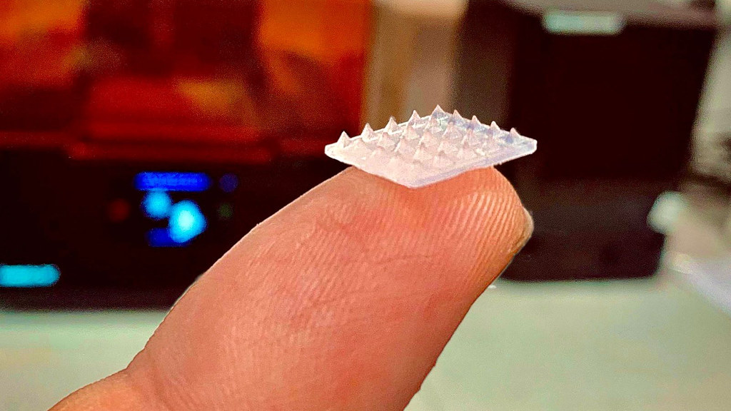 Image of the microneedle skin patch shown on a finger for scale. The patch is about the size of a pound coin.